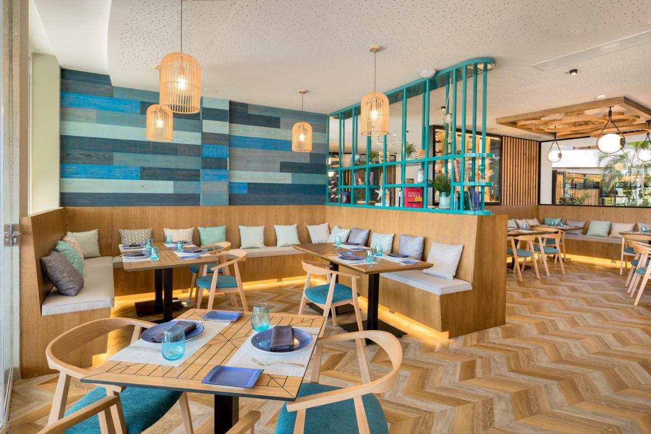 Barcelo Sevilla Renacimiento Esterno foto The photo depicts a modern restaurant interior with a stylish and inviting ambiance. The seating area features a combination of cushioned bench seating along the wall and wooden tables. The walls are decorated with varying shades of blue and wood pan