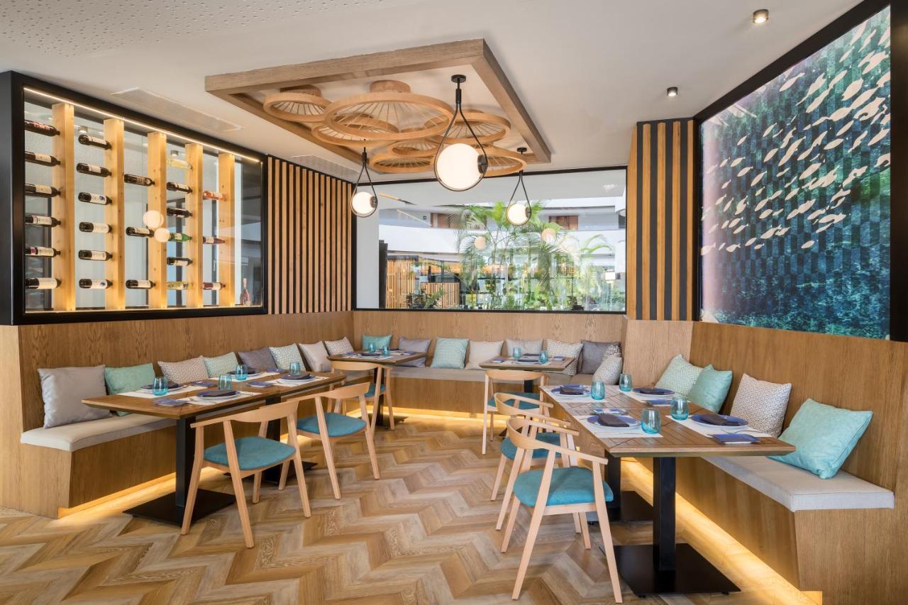 Barcelo Sevilla Renacimiento Esterno foto The photo shows a modern dining area with a stylish and inviting design. It features wooden elements, including a herringbone-patterned floor and wooden walls. There are several tables arranged in a cozy layout, accented by comfortable seating with l