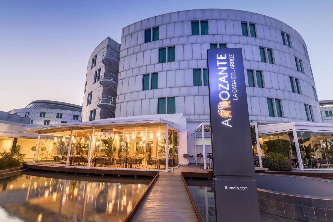 Barcelo Sevilla Renacimiento Esterno foto The photo shows a modern building with a sleek, contemporary design. In the foreground, there is a stylish exterior area with large glass windows and outdoor seating, suggesting it is a restaurant or dining space. A prominent sign reads "Amozanate," 