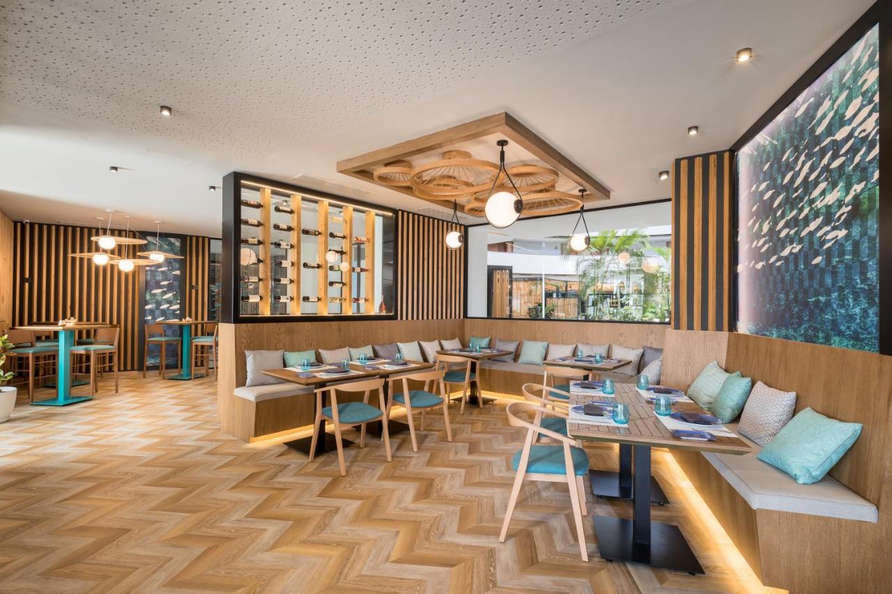 Barcelo Sevilla Renacimiento Esterno foto The photo shows a modern restaurant or café interior featuring a combination of wood and contemporary design elements. There are wooden panels on the walls, and the flooring has a herringbone pattern. Comfortable seating is arranged along the walls w