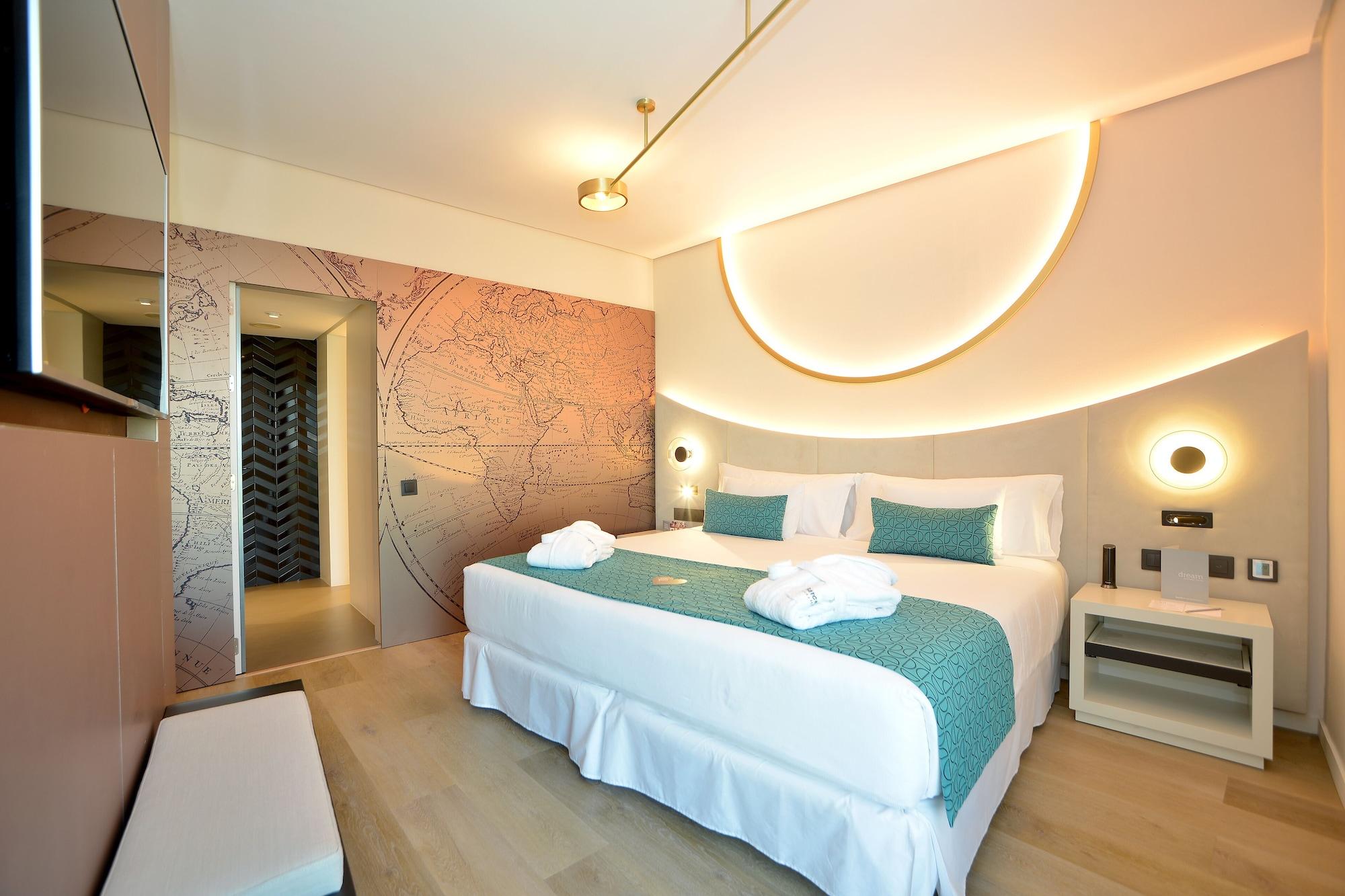 Barcelo Sevilla Renacimiento Esterno foto The photo shows a modern hotel room featuring a large, neatly made bed with a white bedspread and teal throw pillows. The room has a stylish design, with a decorative wall featuring a light-colored map pattern and ambient lighting forming a circular 
