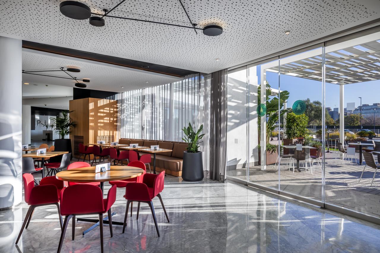 Barcelo Sevilla Renacimiento Esterno foto The photo depicts a modern dining area within a restaurant. It features a combination of tables and cozy seating arrangements. The decor includes red chairs paired with round wooden tables, and a comfortable booth area with a soft sofa in the backgro