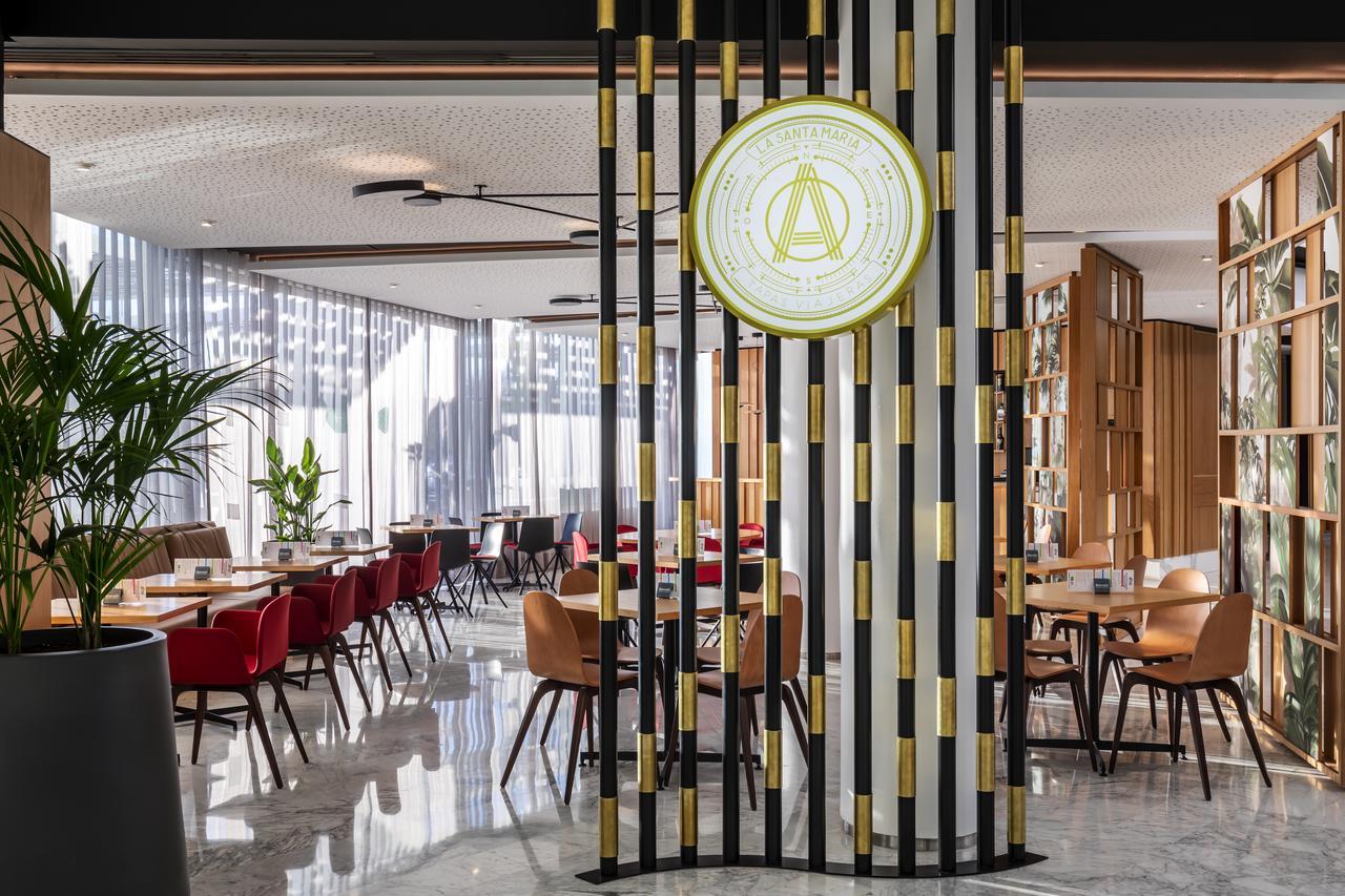 Barcelo Sevilla Renacimiento Esterno foto The photo showcases a modern restaurant interior. It features a stylish design with a mix of wooden and metal materials. There are tables and chairs arranged neatly, some with red upholstery and others in lighter tones. The space is well-lit with lar