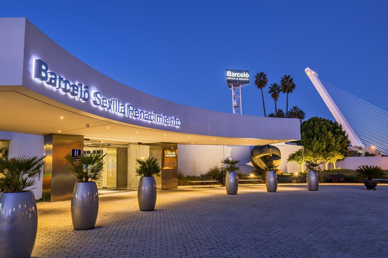 Barcelo Sevilla Renacimiento Esterno foto The photo depicts the entrance of the Barcelo Sevilla Renacimiento hotel. The building features a modern architectural style, with a curved façade and large, illuminated signage. In front of the entrance, there are several planters with palm trees, c